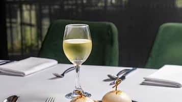 A table with a glass of white wine, two sandwiches, and dining utensils.