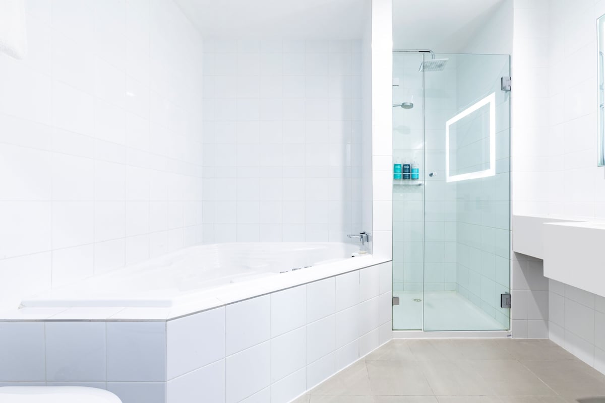 Une salle de bain moderne avec une douche à parois de verre, une baignoire blanche et un meuble-lavabo blanc avec un miroir.