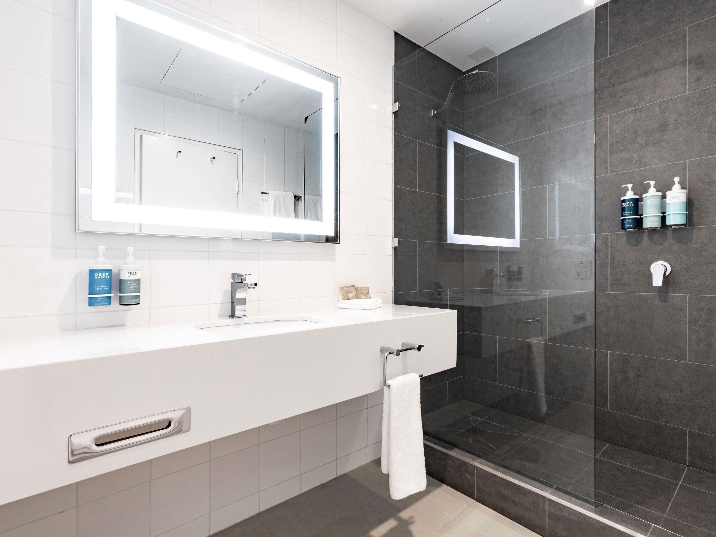 Un baño moderno con un espejo grande, una cabina de ducha de vidrio y artículos de aseo en la encimera.