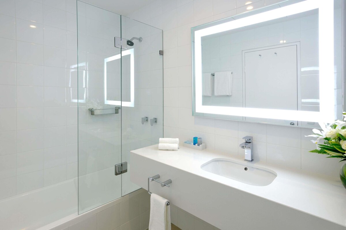 A modern bathroom with a glass shower enclosure, a white sink with a mirror above it, and a towel rack.