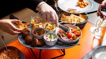 Una mesa de comedor con varios platos, una copa de vino tinto y una persona usando unas pinzas.