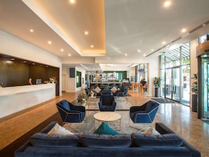 A hotel lobby with a reception desk, seating area with sofas and chairs, a bar, and large windows. - Novotel Melbourne Glen Waverley (Glen Waverley)