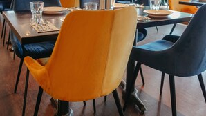 Un restaurante con mesas dispuestas para comer, con una mezcla de sillas azules y anaranjadas.