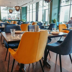 Un restaurante con mesas dispuestas para comer, con una mezcla de sillas azules y anaranjadas.
