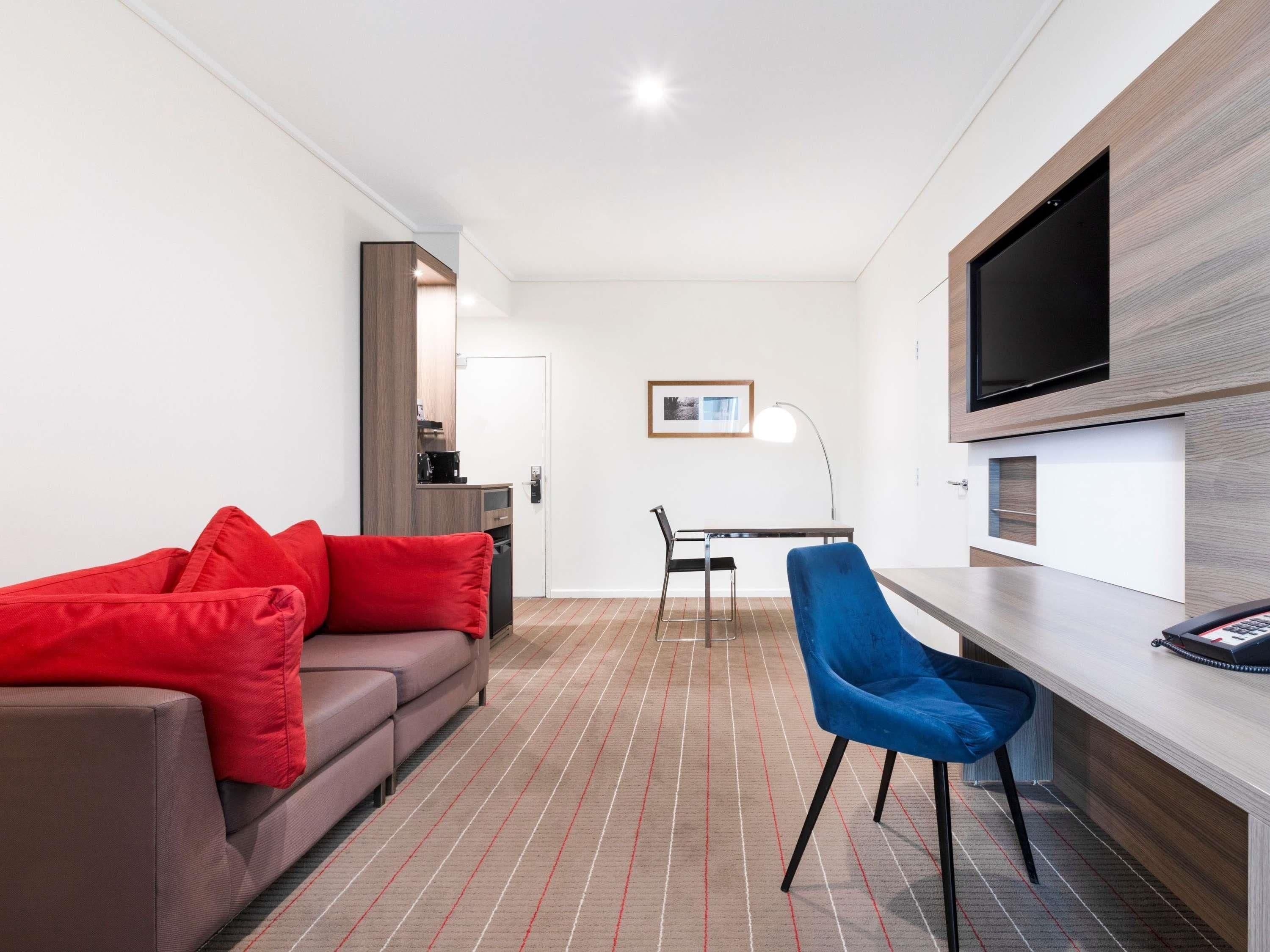 Una habitación de hotel moderna con un sofá, un escritorio, una silla, un televisor y un cuadro en la pared.