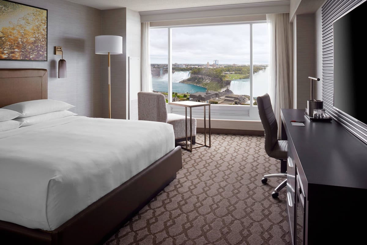 A hotel room with a large bed, a desk, a chair, a lamp, and a view of a waterfall.
