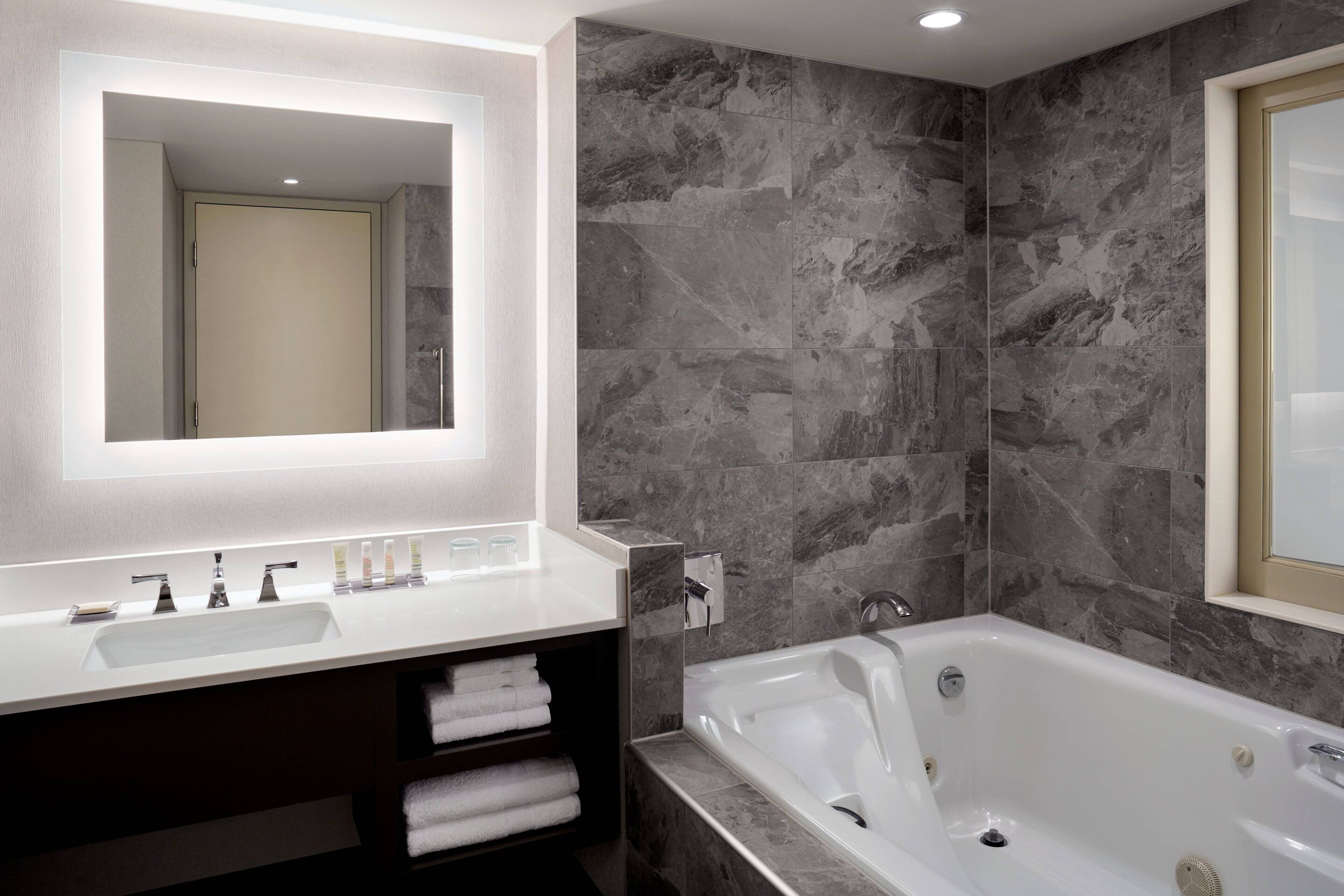 Une salle de bain moderne avec un lavabo blanc, un grand miroir, une baignoire et des murs en marbre.