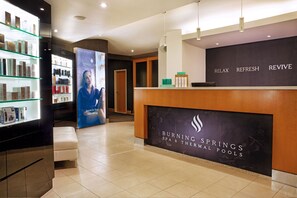 A spa reception area with a reception desk, a glass display of spa products, and a sign for Burning Springs Spa & Thermal Pools.