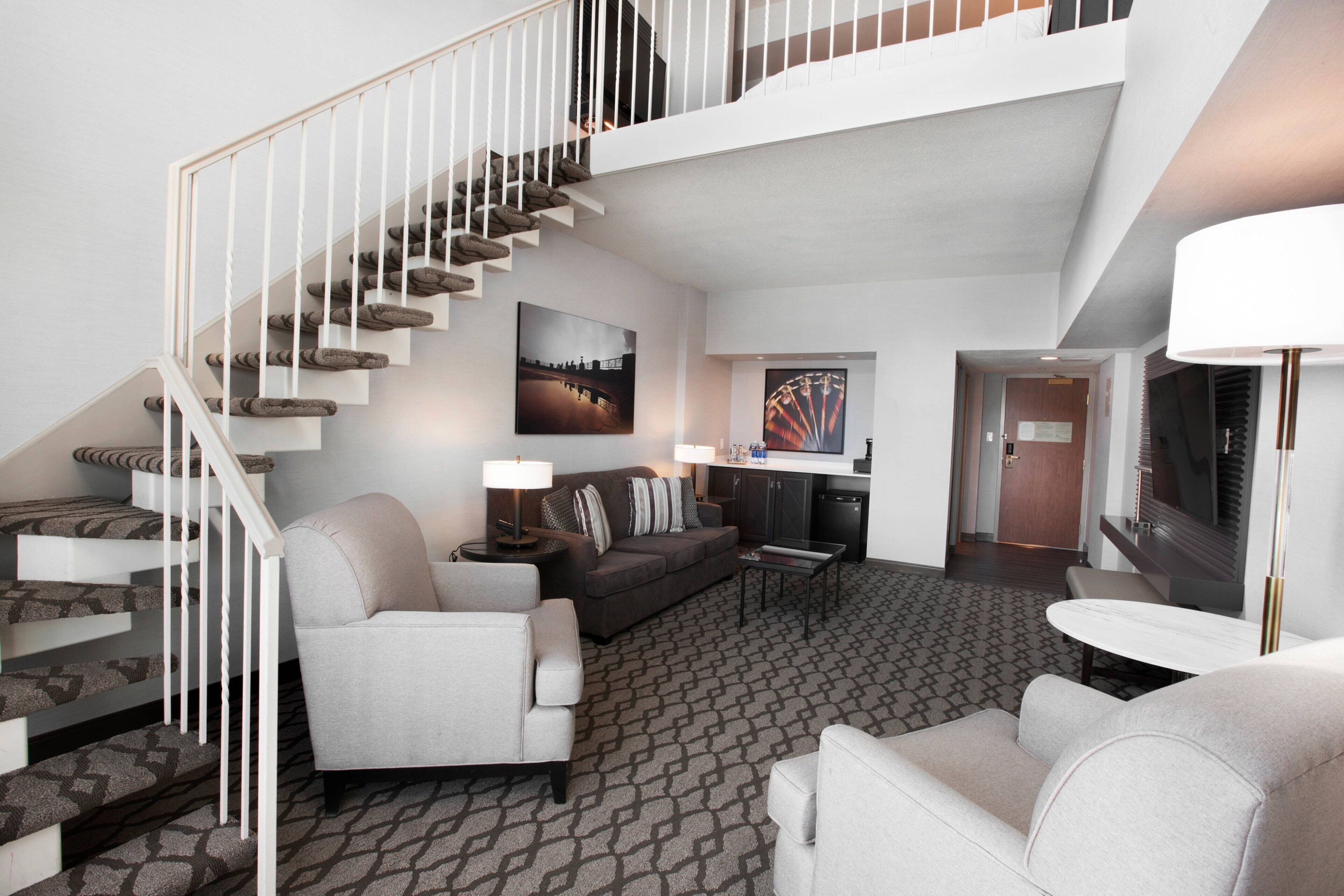 Una habitación de hotel moderna con una escalera, un sofá, una mesa de centro y un televisor.