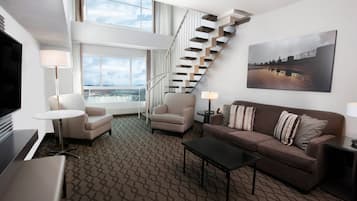 A modern hotel room with a staircase, a sofa, a coffee table, and a TV.