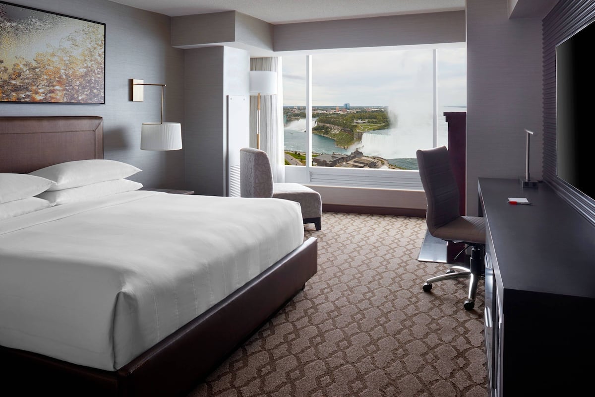 A hotel room with a large bed, a desk, a chair, and a view of a waterfall.