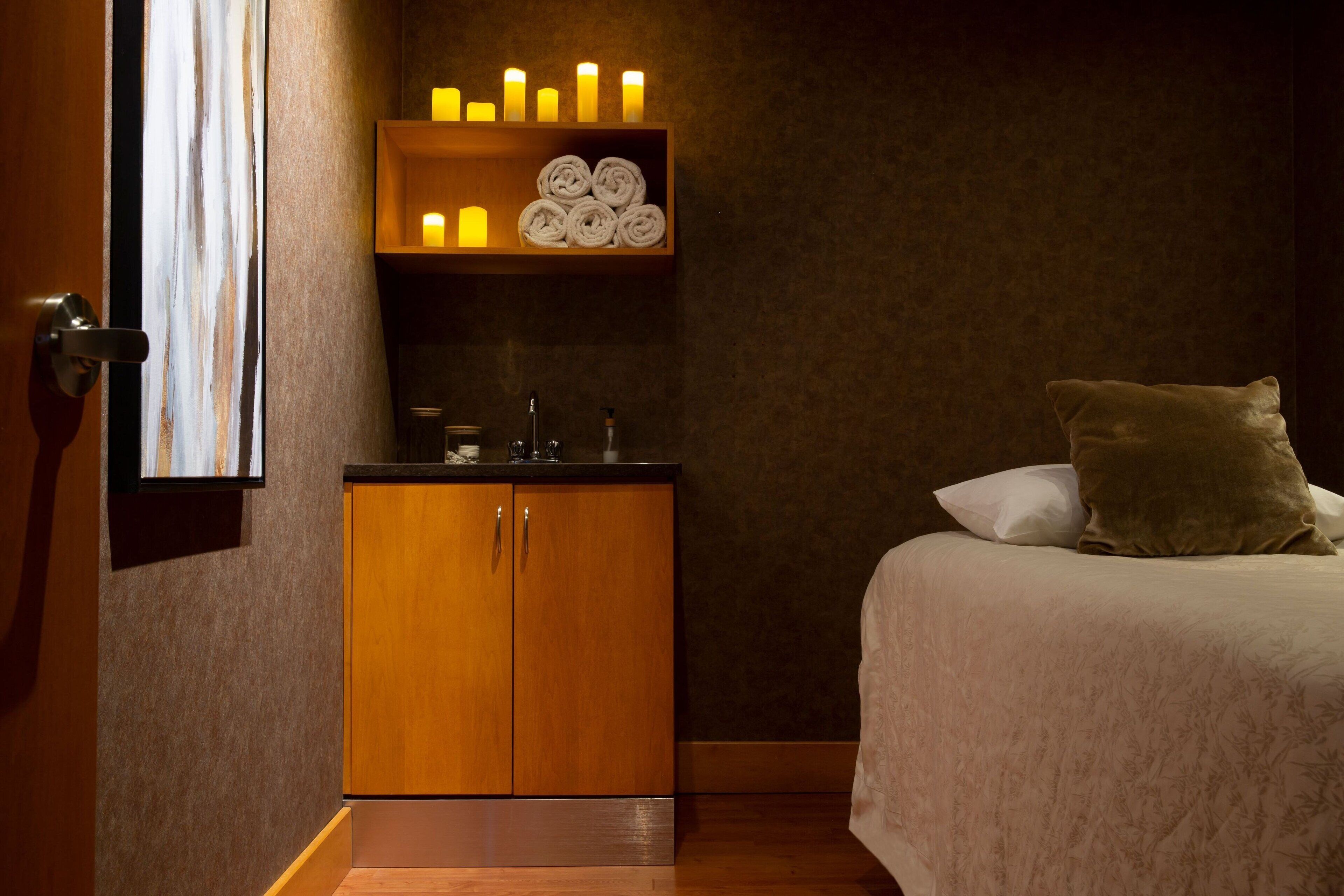 A hotel room with a bed, a wooden cabinet, a shelf with candles, and a window.
