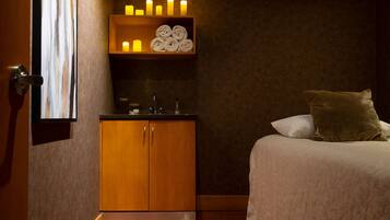 A hotel room with a bed, a wooden cabinet, a shelf with candles, and a window.