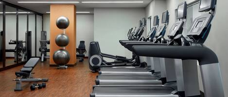 A gym with multiple treadmills, weight machines, and a bench.