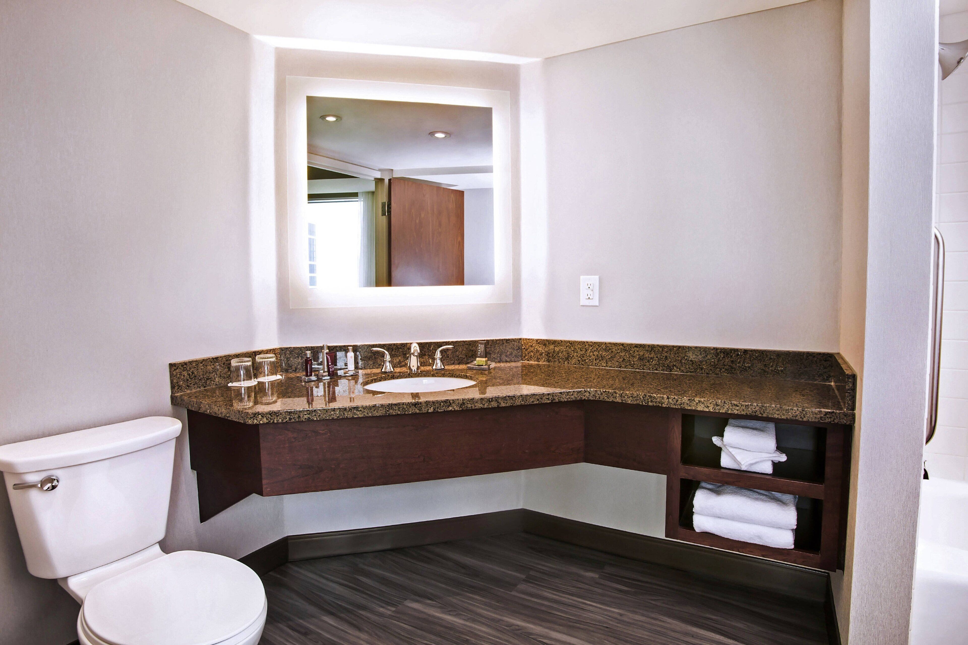 A modern bathroom with a white toilet, a granite countertop sink, and a built-in shelf with towels.