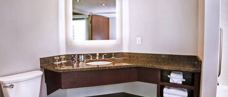 Un baño moderno con inodoro blanco, lavamanos de encimera de granito y un estante empotrado con toallas.