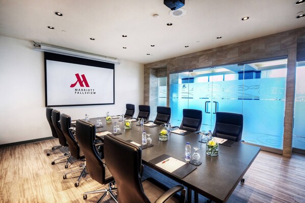 A conference room with a long table, black chairs, water bottles, and a projector screen displaying the Marriott logo.