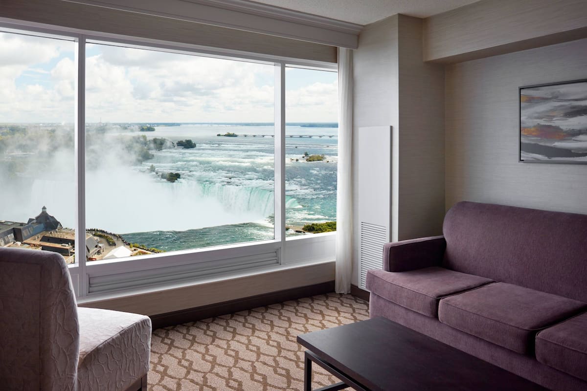 A room with a large window offering a view of a waterfall and distant landscape.