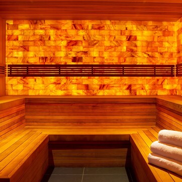 A sauna with wooden benches and a bench seat, a bench with a towel, and a wall with a heat source.