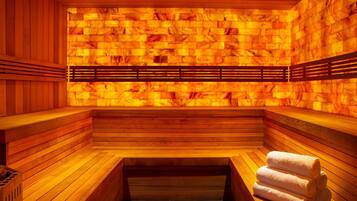 A sauna with wooden benches and a bench seat, a bench with a towel, and a wall with a heat source.