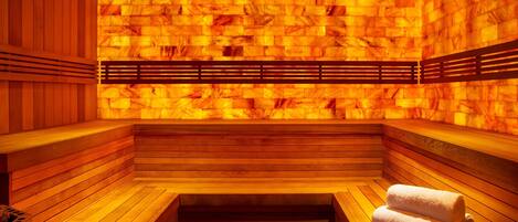 A sauna with wooden benches and a bench seat, a bench with a towel, and a wall with a heat source.