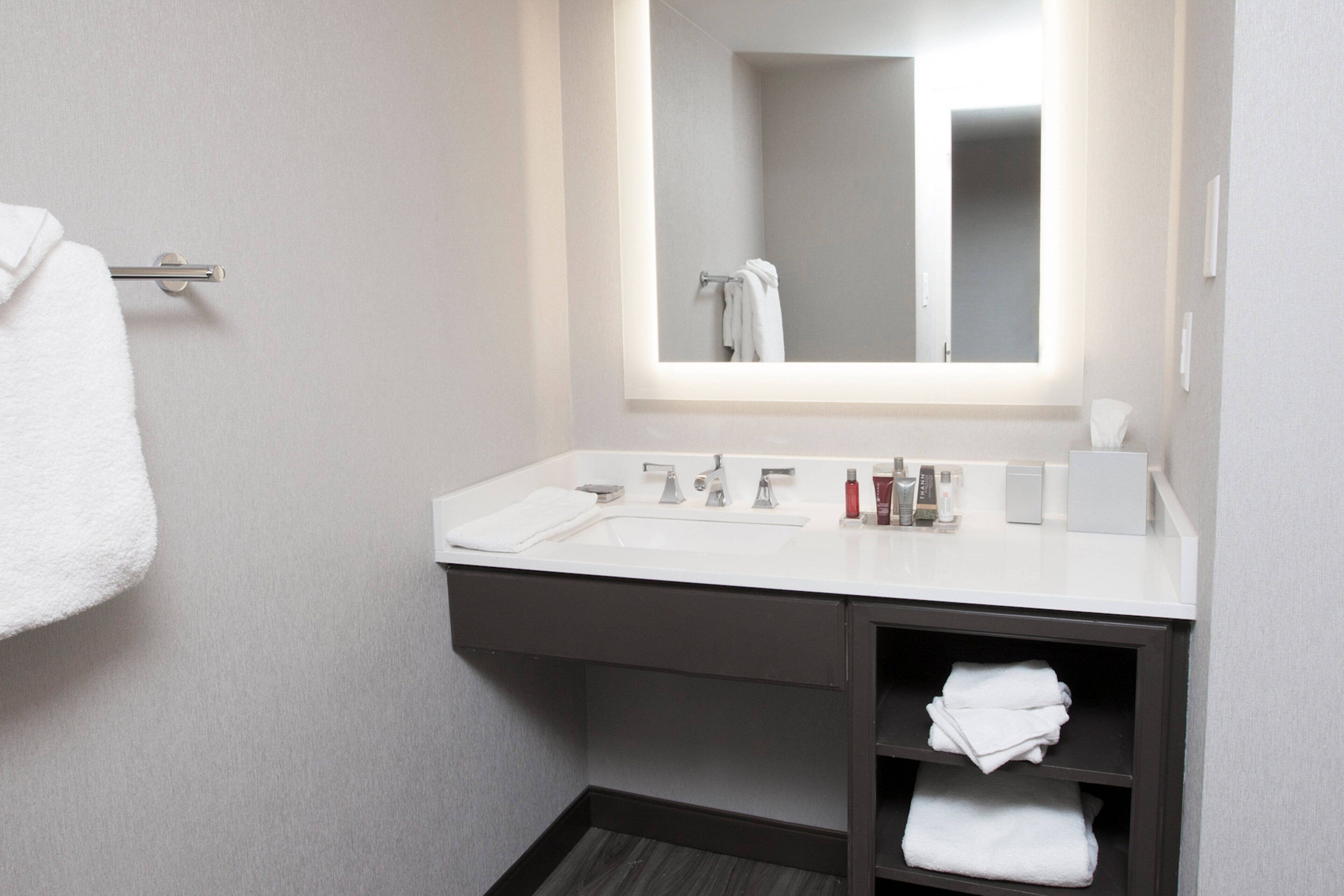 Un baño moderno con un lavamanos blanco, un espejo grande y un perchero para toallas.