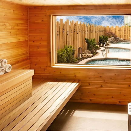 A wooden sauna room with a bench, towels, a window view of a pool and garden, and a stone basin.