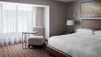 Habitación de hotel con una cama grande, una mesita, una silla, una lámpara y un cuadro en la pared.