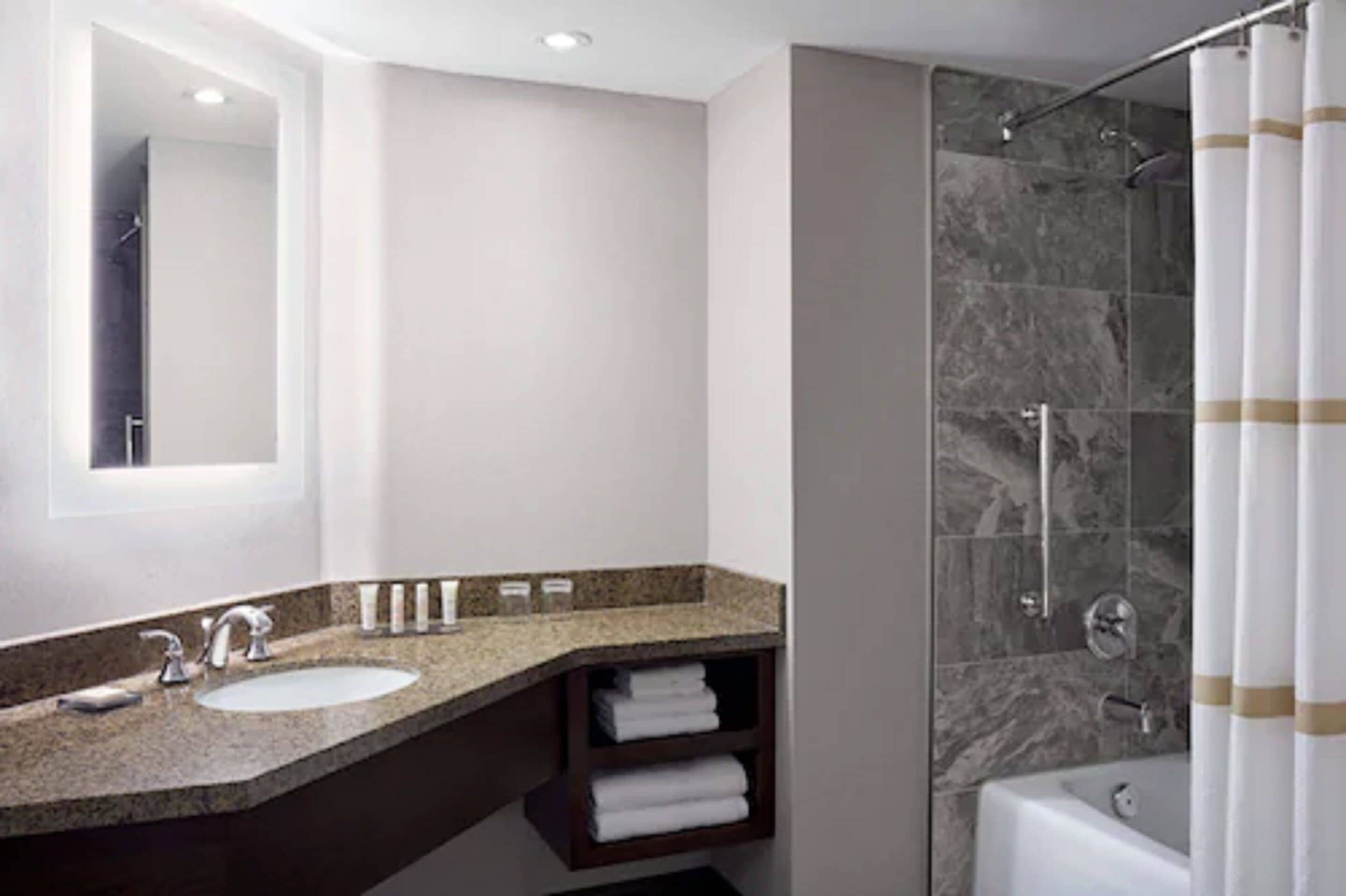 Un baño moderno con encimera de granito, lavamanos, espejo, ducha con puerta de vidrio y bañera.