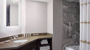 Un baño moderno con encimera de granito, lavamanos, espejo, ducha con puerta de vidrio y bañera.