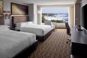 A hotel room with two beds, a desk, a chair, a TV, and a large window with a view of a waterfall.
