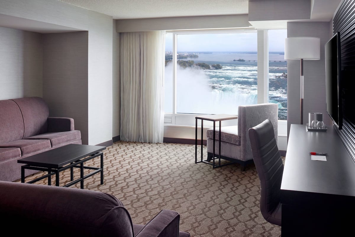 A hotel room with a large window offering a view of the ocean, a sofa, a desk, and a chair.