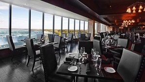 A restaurant with tables set for dining, large windows offering a view of a waterfall, and modern lighting fixtures. - Marriott Niagara Falls Fallsview Hotel & Spa (Niagara Falls)
