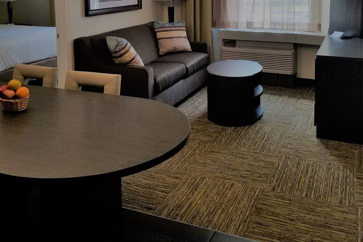 Une chambre d’hôtel avec un lit, un canapé, une table ronde avec des fruits, une télévision et une fenêtre avec des rideaux.