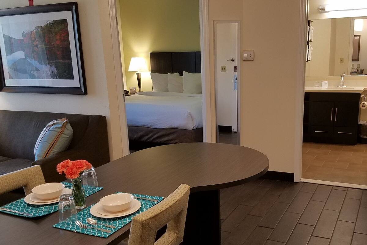Une chambre d’hôtel comprenant un coin repas, un lit et une salle de bain, le tout visible à travers une porte ouverte.