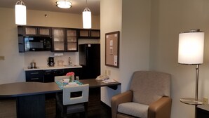 A compact kitchen with a microwave, refrigerator, and a small island with a sink. There is a chair and a lamp near the kitchen.