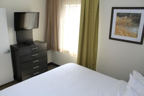 Un cuarto de hotel con una cama, un televisor en una cómoda, una ventana con cortinas y un cuadro en la pared.