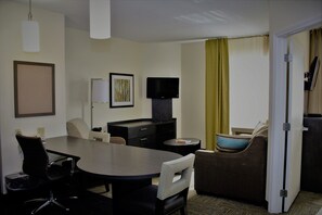 Une chambre d’hôtel comprenant une table à manger, deux chaises, un canapé, une télévision, un bureau et une porte.