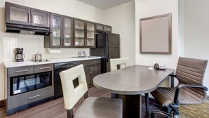 A modern kitchen with dark cabinets, a built-in oven, and a large dining table with chairs.