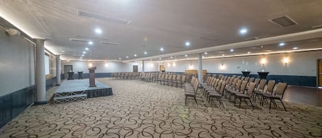 Une grande salle de conférence dotée d’un tapis à motifs, de rangées de chaises, d’une scène et d’un pupitre.
