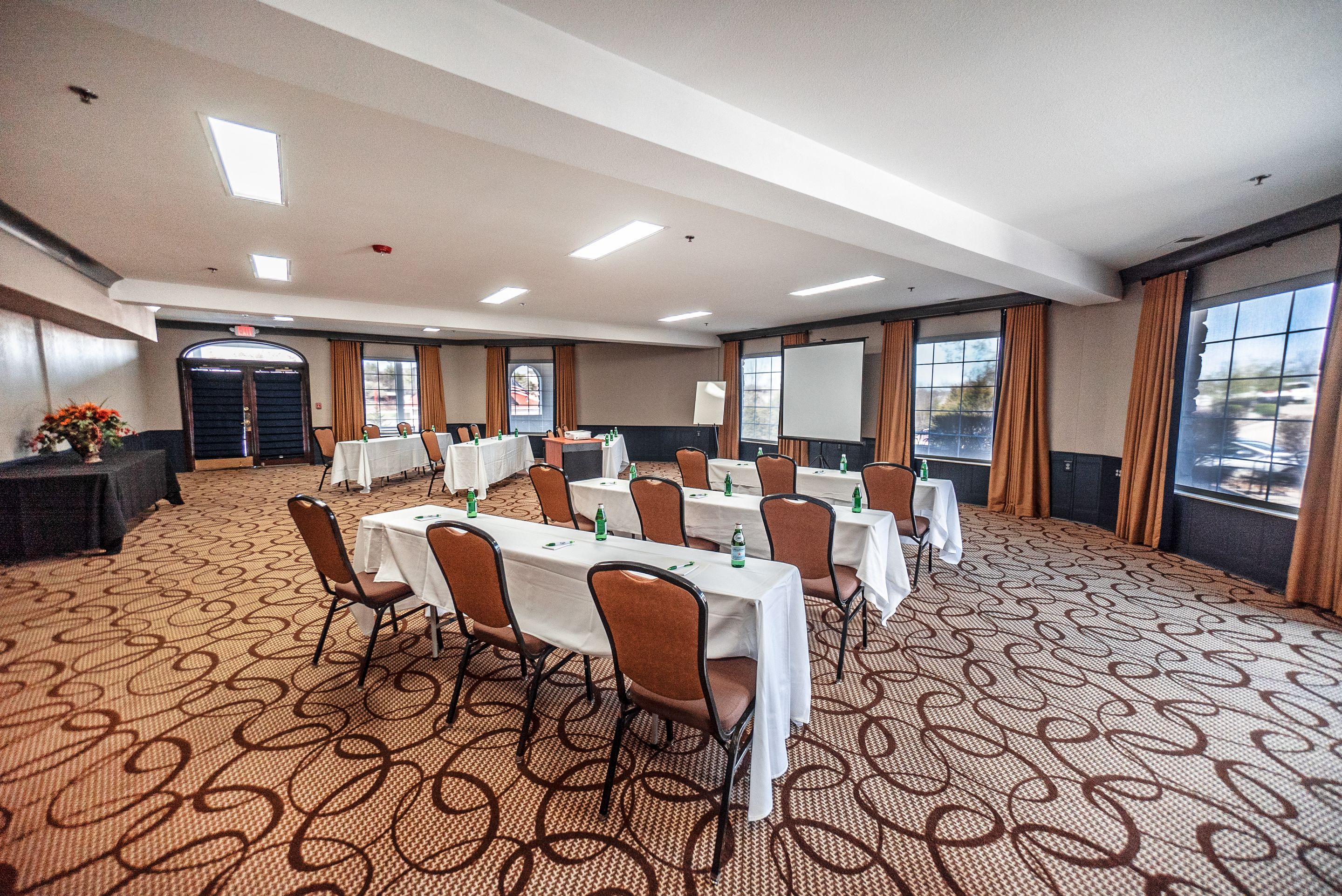 A conference room with tables and chairs, a projector screen, and a carpeted floor.
