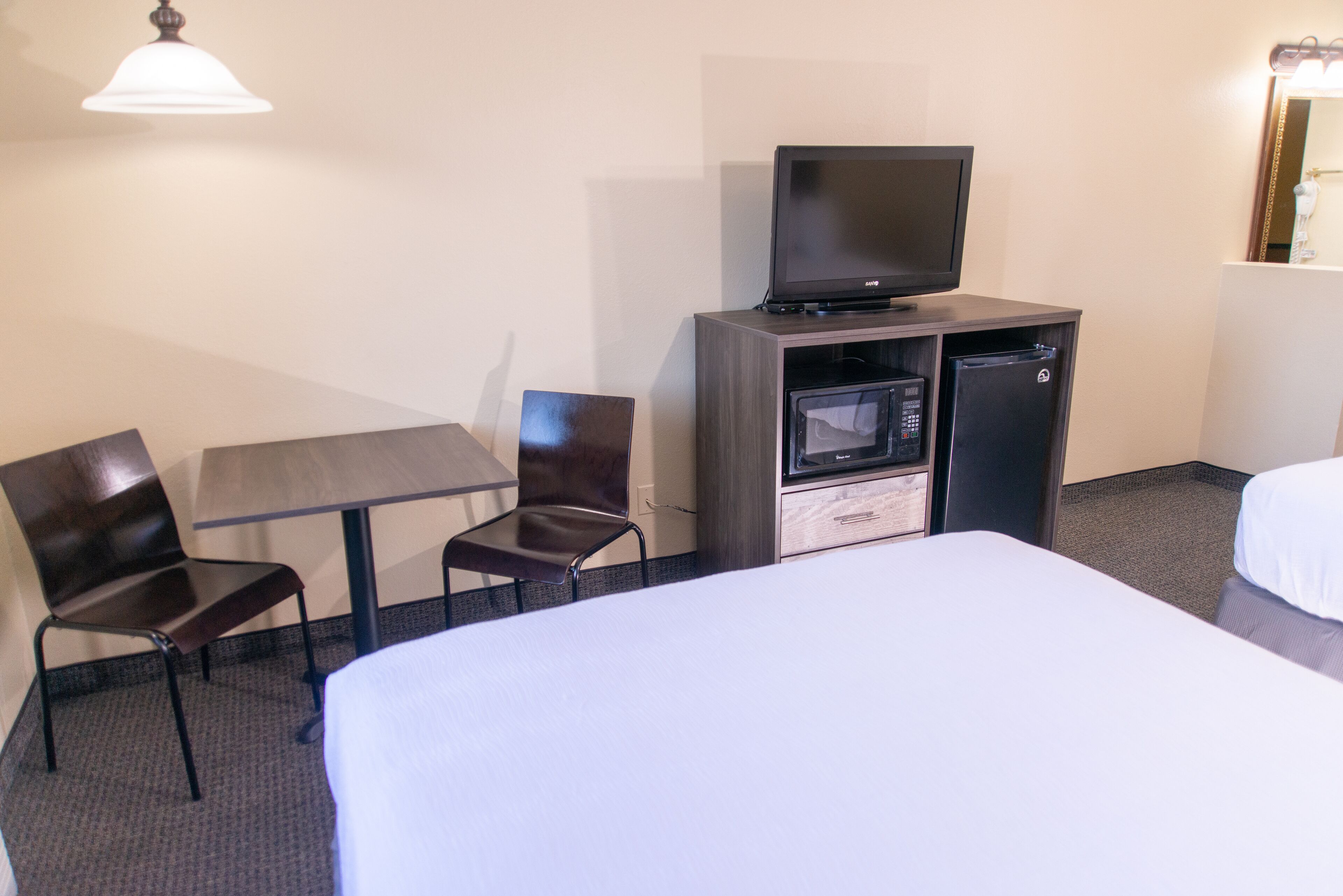 A hotel room with a bed, a desk with a chair, a television, and a mini-fridge.