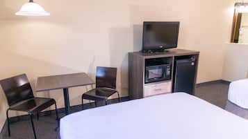 Habitación de hotel con cama, escritorio, silla, televisión y un mini refrigerador.