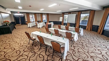 A conference room with multiple tables and chairs, a whiteboard, and a projector screen.