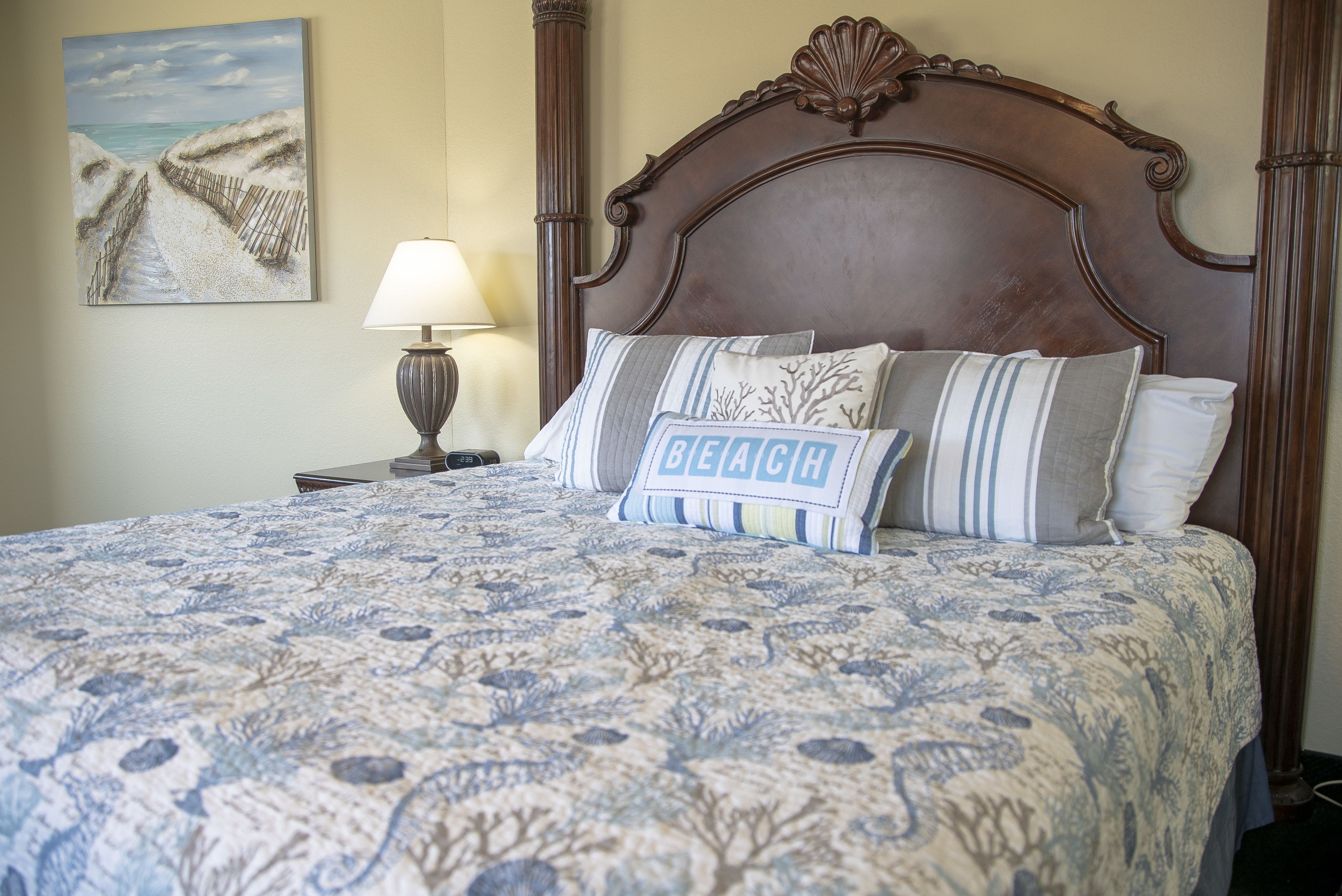 Una cama con un edredón estampado, un cabecero y almohadas, incluyendo una con la palabra 'BEACH'.