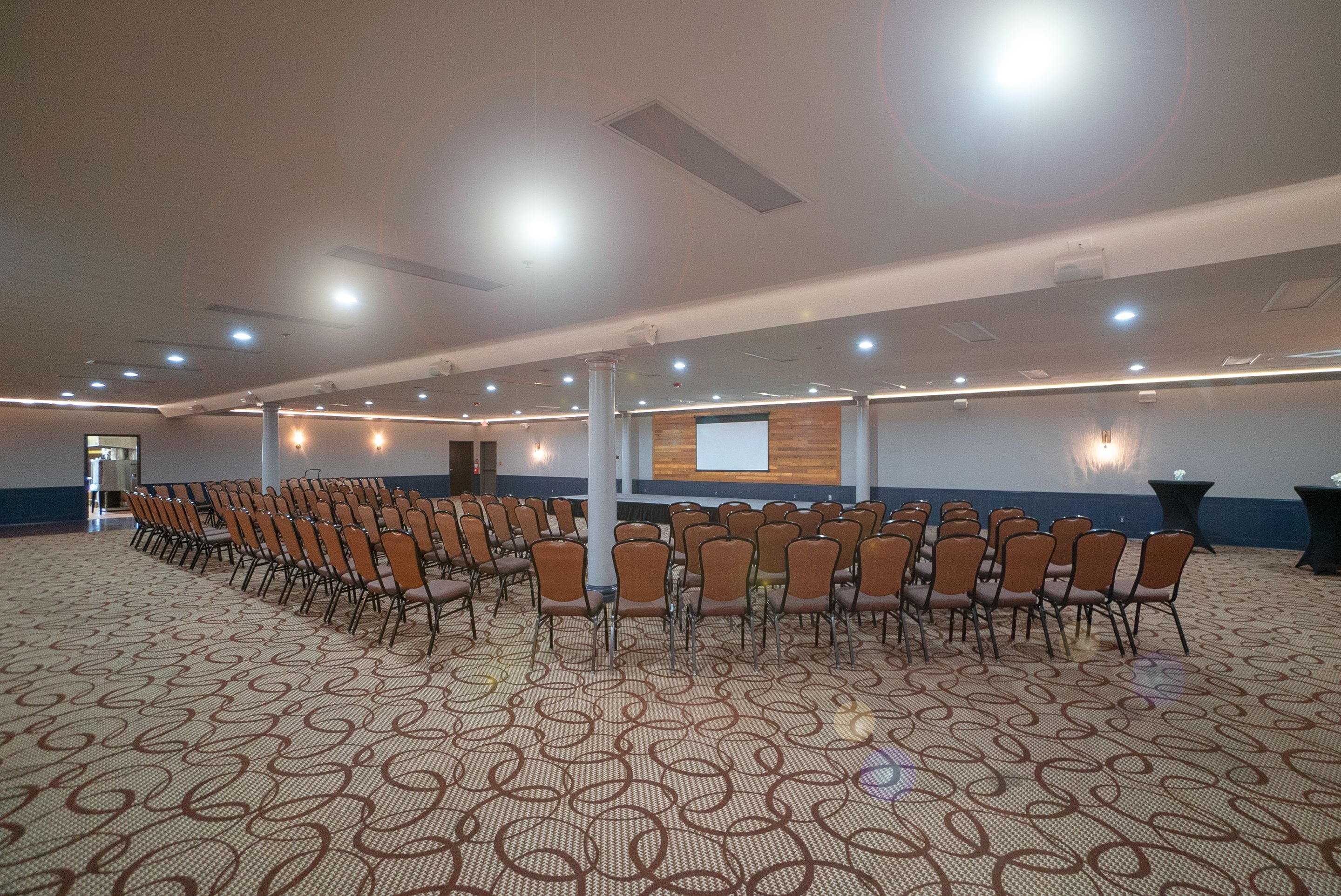 A conference room with rows of chairs, a projector screen, and a patterned carpet.