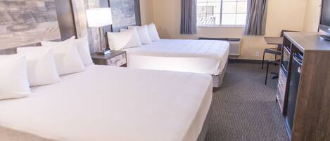 A hotel room with two beds, a desk, a chair, a TV, and a window with curtains.