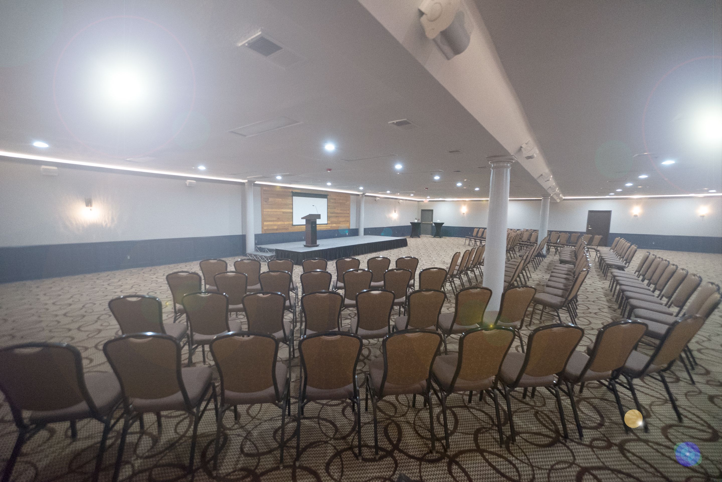 A conference room with rows of chairs, a podium, and a carpeted floor.