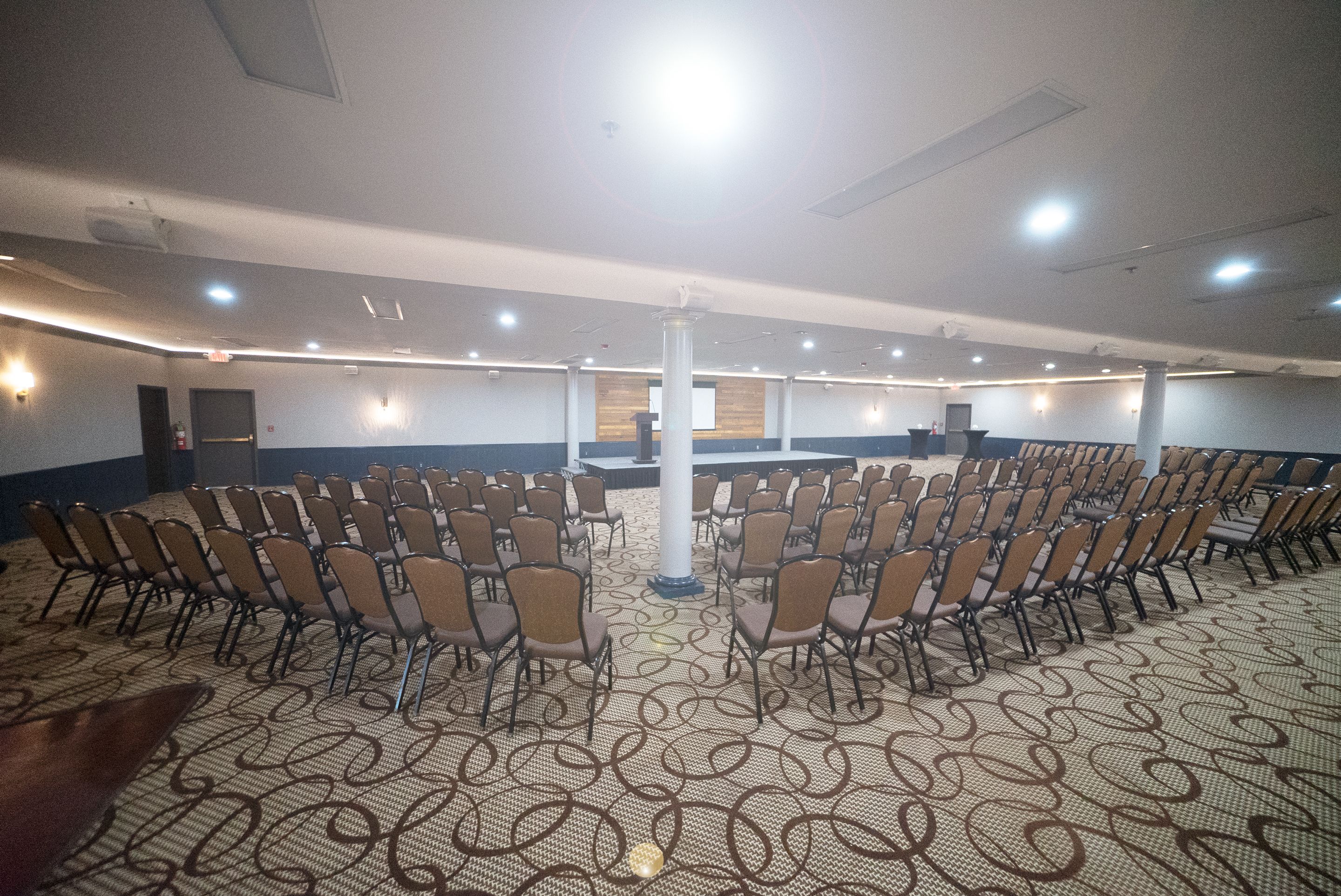 A conference room with rows of chairs, a stage, and a patterned carpet.