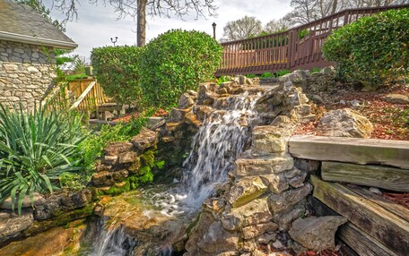 A small waterfall in a landscaped garden with stone walls and wooden railings.